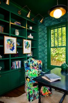 a room with green bookshelves and a chair in front of a window that has pictures on it