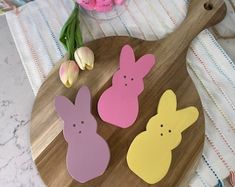 three wooden easter bunnies sitting on top of a cutting board next to tulips