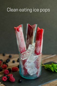 a glass filled with ice and raspberries on top of a wooden table next to berries