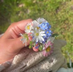 a person holding flowers in their hand on top of a stone slab outside with grass