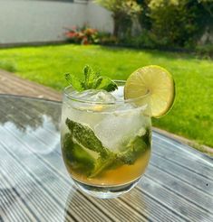 a close up of a drink on a table with grass and trees in the background