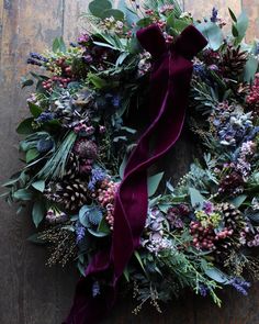 a wreath with purple and green flowers, greenery and berries on it is hung on a wooden surface