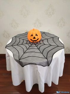 a pumpkin sitting on top of a table with a spider web covering it's face