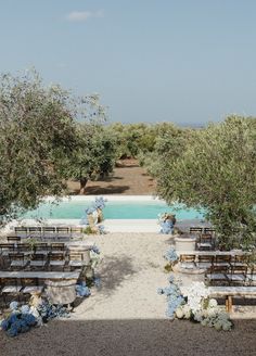 an outdoor ceremony setup with blue flowers and greenery on the aisle, surrounded by olive trees