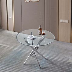 a glass table with silver legs in front of a wall mounted mirror and door to another room