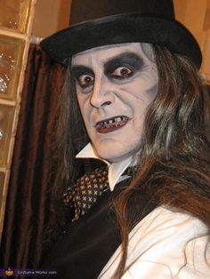 a man with long hair wearing a black top hat and white face paint is posing for the camera