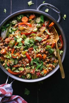 a pan filled with rice and vegetables on top of a wooden table next to a fork