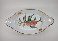 a white and gold serving dish with fruit painted on the side, sitting on a table