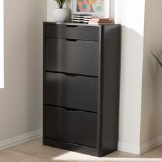 a black dresser with three drawers in front of a white wall and potted plant