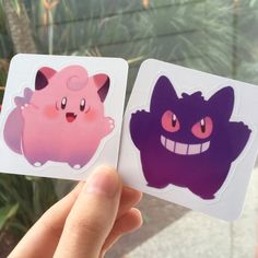 someone is holding up two stickers with different designs on them, one pink and the other purple