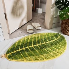 a bathroom with a green leaf rug on the floor and slippers next to it