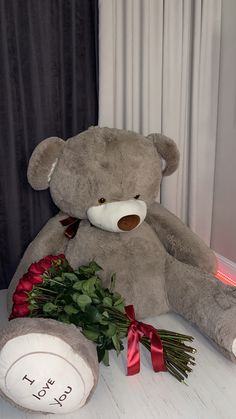 a large teddy bear sitting on top of a table next to a bouquet of roses