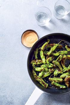 a pan filled with green peppers next to two glasses and sauces on the side