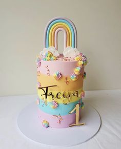 a birthday cake decorated with rainbows, clouds and a number one on it's side