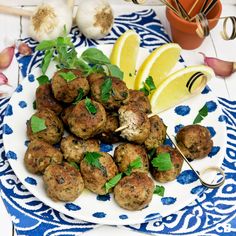 a plate with meatballs and lemon wedges on it next to garlic, parsley and herbs