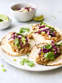 three tortillas with shredded cabbage and cilantro are on a white plate