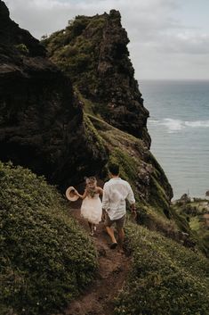 a man and woman walking down a path next to the ocean