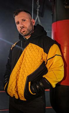 a man in a yellow and black jacket standing next to a punching bag with his hands on his hips