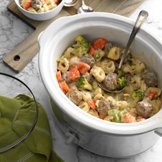 a pot filled with pasta and meatballs on top of a marble counter next to a wooden cutting board