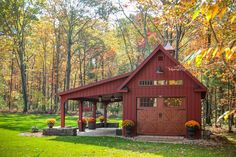 a red barn with a covered porch in the middle of some trees and foliage around it