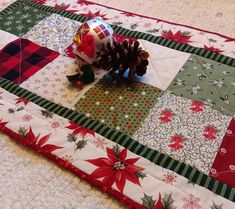 a quilted christmas table runner with a pine cone and ornaments on the top one