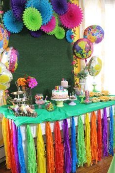 there is a table that has many colorful decorations on it and balloons in the background