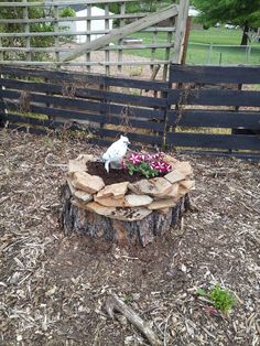 a bird statue sitting on top of a tree stump in the middle of a yard