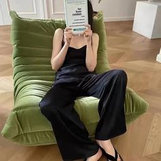 a woman sitting on a green couch holding up a book in front of her face