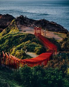 an aerial view of people walking on a red bridge over the ocean and hills in the background