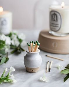 a white vase filled with matchsticks on top of a table next to flowers