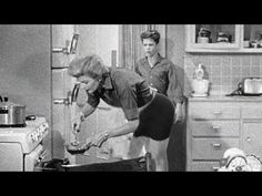 two women are in the kitchen and one is bending over to look at something on the stove