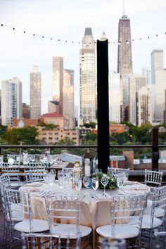 an outdoor table set up with white linens and place settings in front of the city skyline