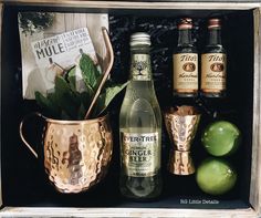 an open wooden box filled with alcohol bottles and green apples next to other liquors