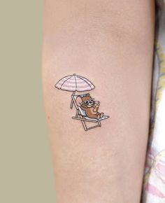 a small tattoo on the arm of a person sitting in a beach chair under an umbrella