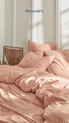 an unmade bed with pink sheets and pillows in front of a window that reads bonsors