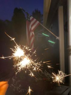 a person holding a sparkler in their hand and an american flag on the other side