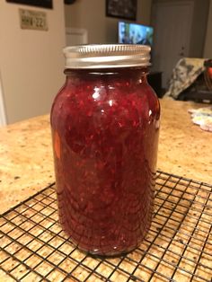 a jar filled with red liquid sitting on top of a counter next to a wire rack