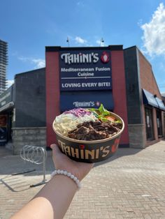 a person holding up a bowl of food in front of a building with a sign