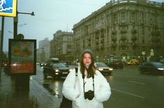 a woman standing on the side of a road in front of some buildings and cars