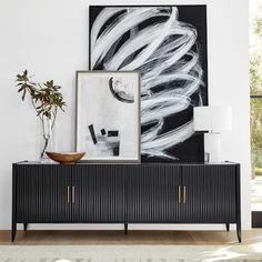 a black and white painting hangs on the wall next to a sideboard