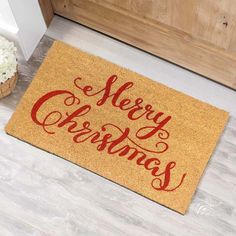 a door mat that says merry christmas on it next to a vase with white flowers