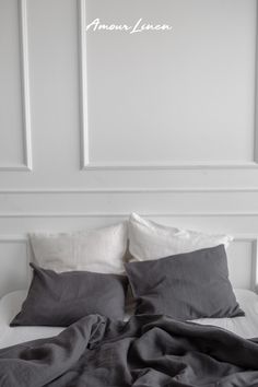 an unmade bed with white sheets and gray blankets on it in front of two framed pictures