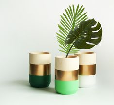 three vases with green, white and gold stripes on the bottom one has a plant in it