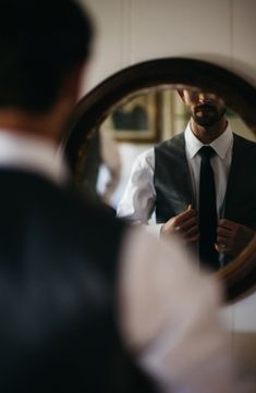 a man in a vest and tie is looking at himself in the mirror