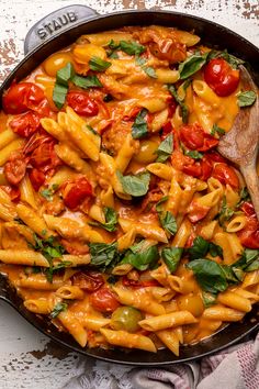 a skillet filled with pasta, tomatoes and spinach on top of a table