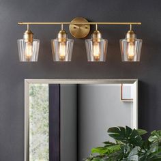 a bathroom vanity with three lights and a mirror on the wall next to a potted plant