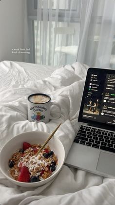 an open laptop computer sitting on top of a bed next to a bowl of cereal