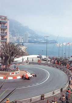 a race track with cars driving on it and people watching from the sidelines looking out over the water