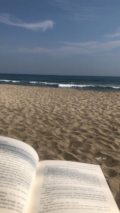 an open book sitting on top of a sandy beach