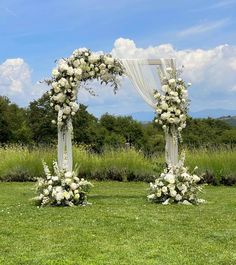 an outdoor wedding ceremony setup with white flowers and greenery on the grass in front of a blue sky